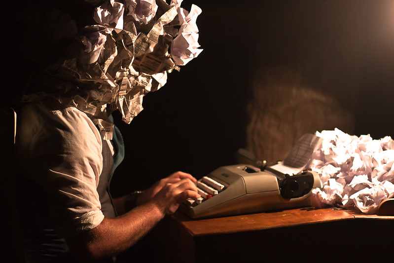WritersBlock Man sits at a typewriter with a screwed up piece of paper for a head