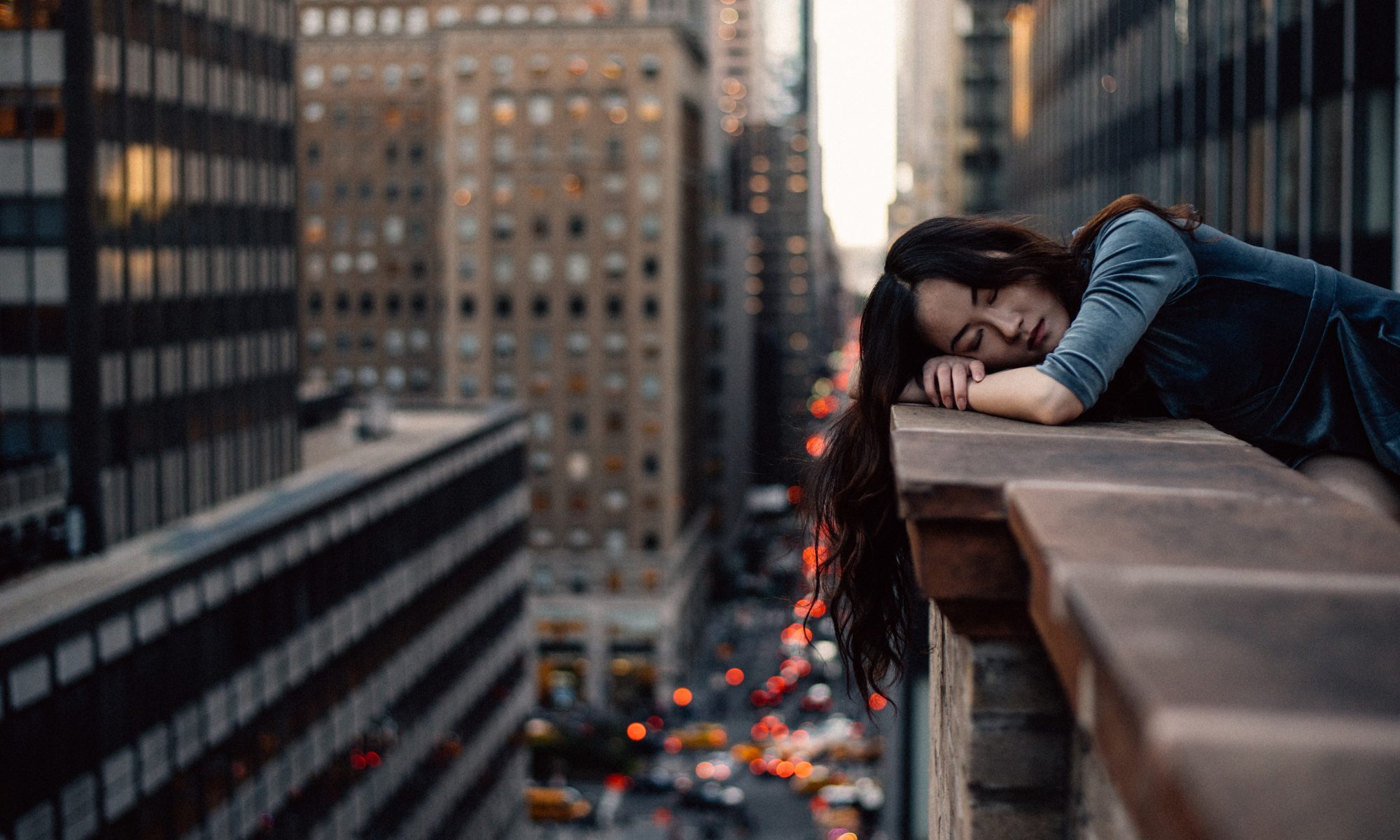 A Woman rests on a wall overlooking a busy street