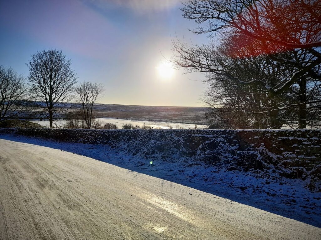 A snowy countryside road overlooking an ice-covered Redmires Reservoir | Photo by H Fenoughty